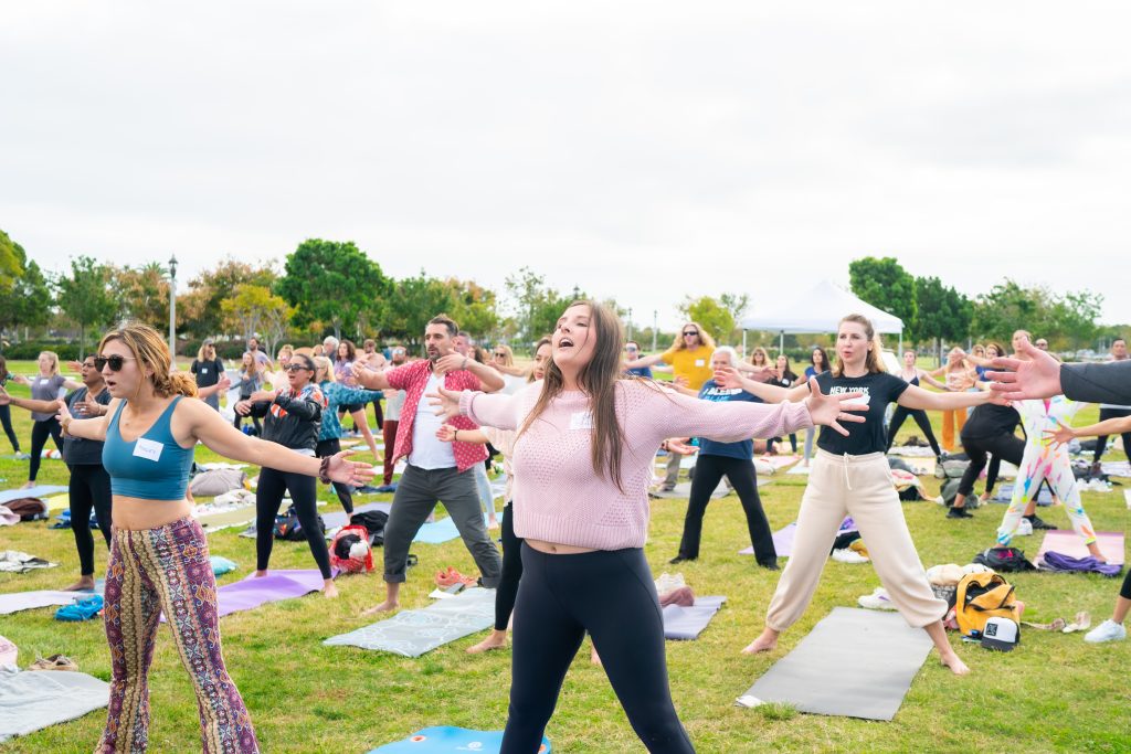 crowd with yoga mats standing with their arms stretched wide